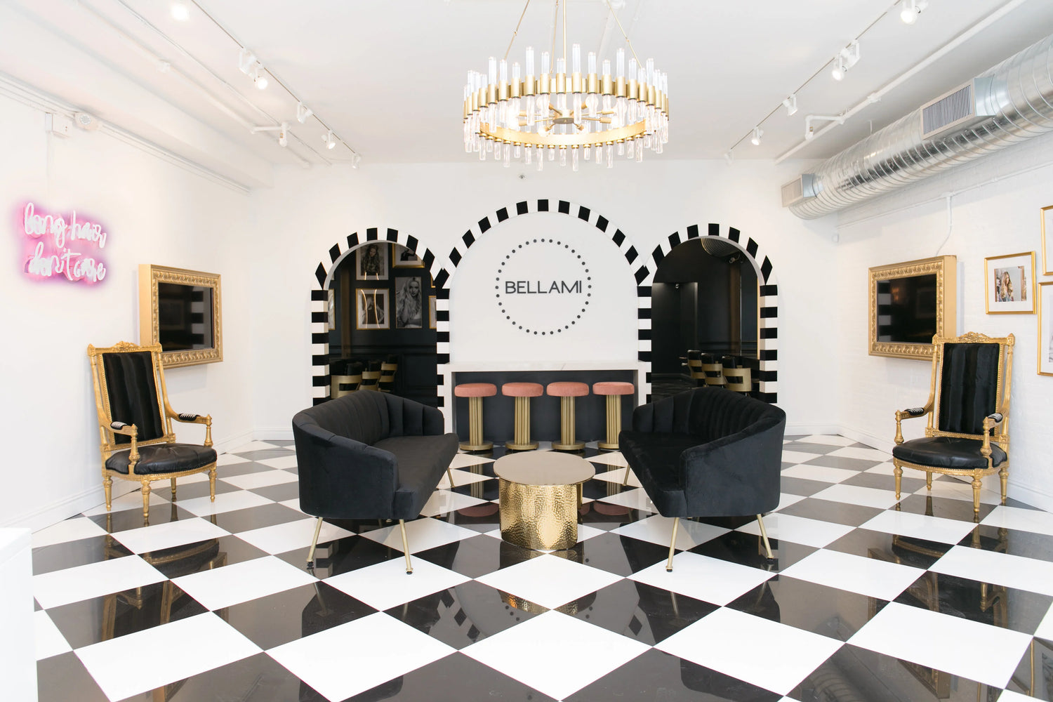 Chic salon with checkered floor, black velvet seating, gold chandelier, neon sign "long hair, don’t care," and Bellami logo.