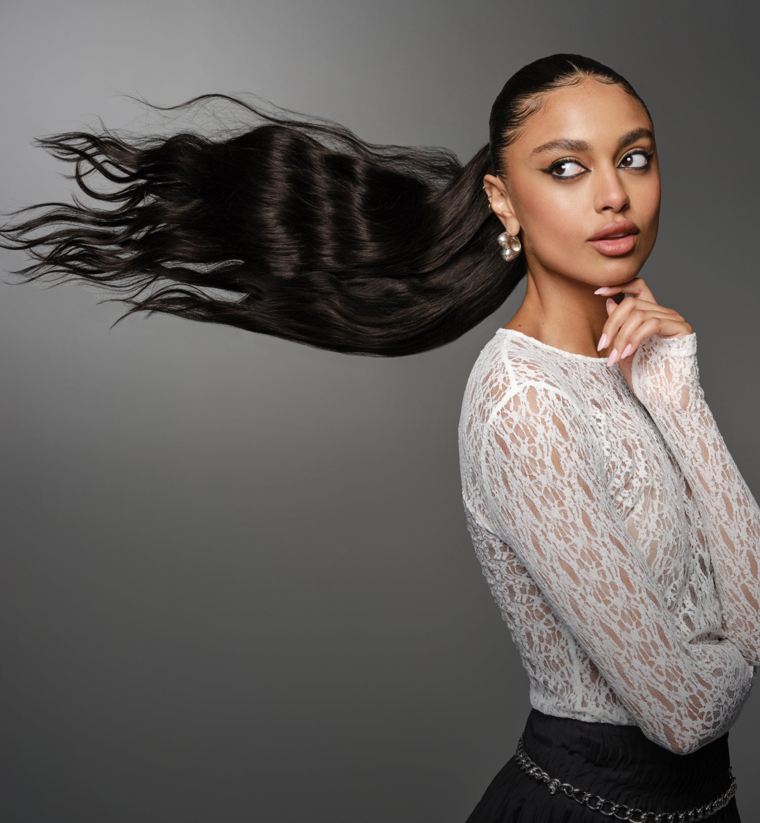 A woman with long hair in a lace top is positioned in front of a dark grey backdrop.