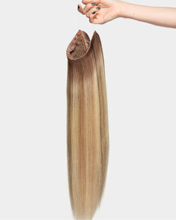 A hand holding a BELLAMI Halo PRO Hair Extensions Kit weft by its invisible wire in Vanilla Latte Highlight, showing the weft's length and movement.