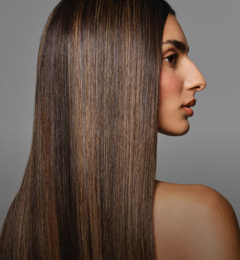 Side profile of a woman with sleek, straight brunette hair and subtle highlights, emphasizing smooth texture and shine.