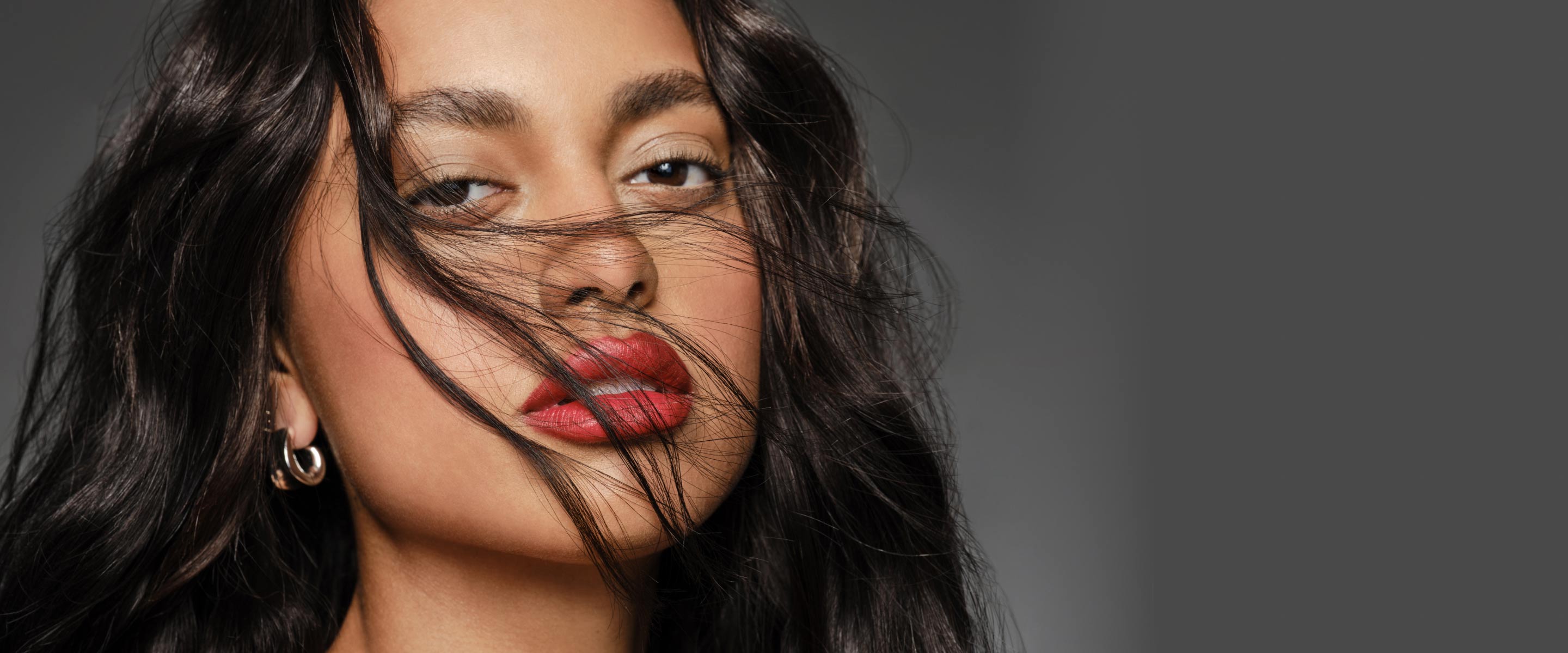 A woman hair flowing showcasing wavy long black hair extensions, complemented by bold red lipstick.